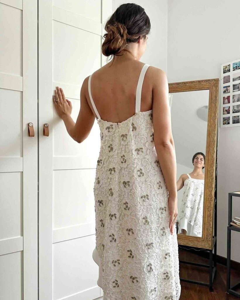 Visto da dietro, Il cambio d'abito da sposa di Elena è un abito asimmetrico con spalline e scollatura dritta realizzato con un tessuto ricamato con perline