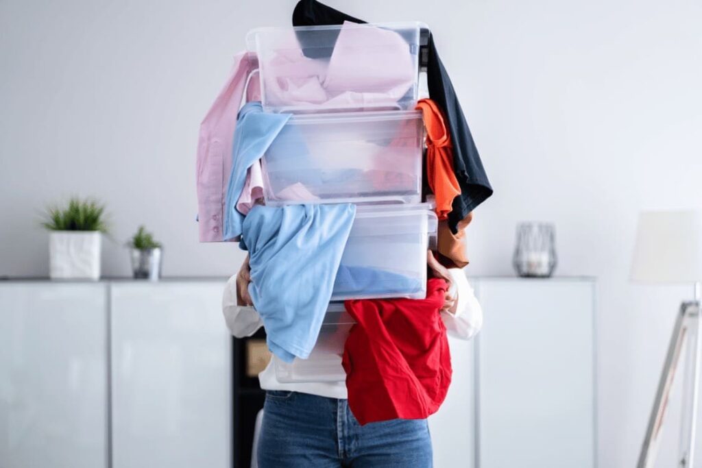 una ragazza con molti vestiti in delle scatole dopo il decluttering dell'armadio